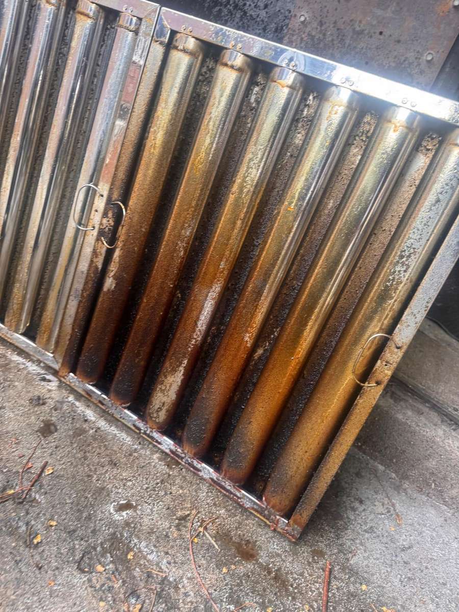 Filtres chicane de hotte déposés à l'extérieur, saturés de graisse orangée et de rouille